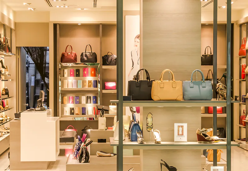 Tienda con bolsos y calzado exhibidos en estanterías iluminadas.